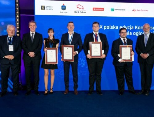 Zdjęcie grupowe laureatów i organizatorów X polskiej edycji Konkursu 'Etyka w finansach'. Pięć osób w centralnej części kadru trzyma oprawione dyplomy, stojąc na tle niebieskiej ścianki z logotypami partnerów konkursu, m.in. Związku Banków Polskich, Banku Pekao, PKO Banku Polskiego, Santander Bank Polska, BNP Paribas i innych. Laureaci ubrani są formalnie – kobieta w eleganckiej czarnej sukience, mężczyźni w garniturach. Po bokach stoją czterej starsi mężczyźni – członkowie jury oraz przedstawiciele instytucji wspierających.